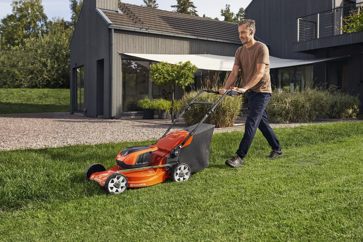 A man mowing a lawn with Husqvarna LC142i Lawn Mower in front of a modern house with a large garden