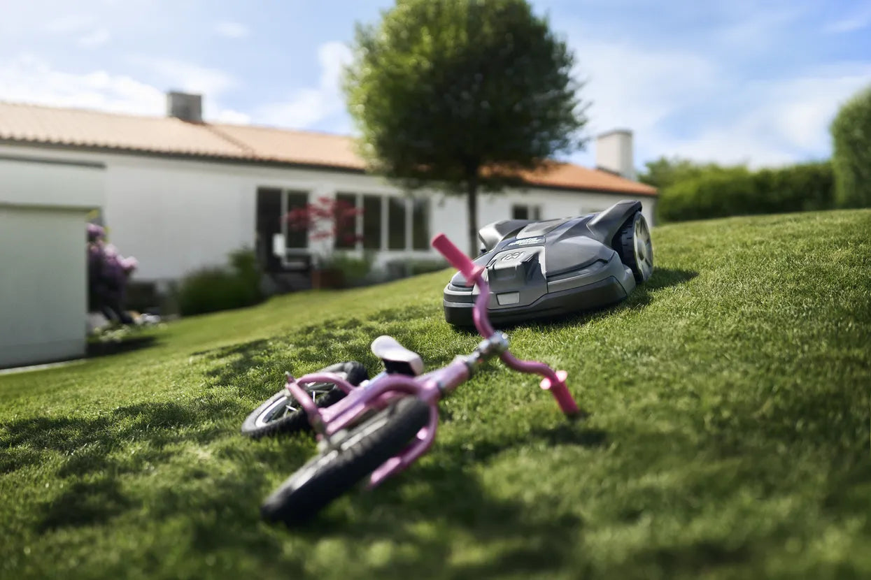 Husqvarna 430X NERA Automower® working with a pink bicycle laying on a turf grass